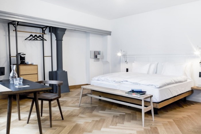 A spacious room in Zürich’s Marktgrasse Hotel, with parquet flooring, plain white walls a large bed and an open iron-framed wardrobe