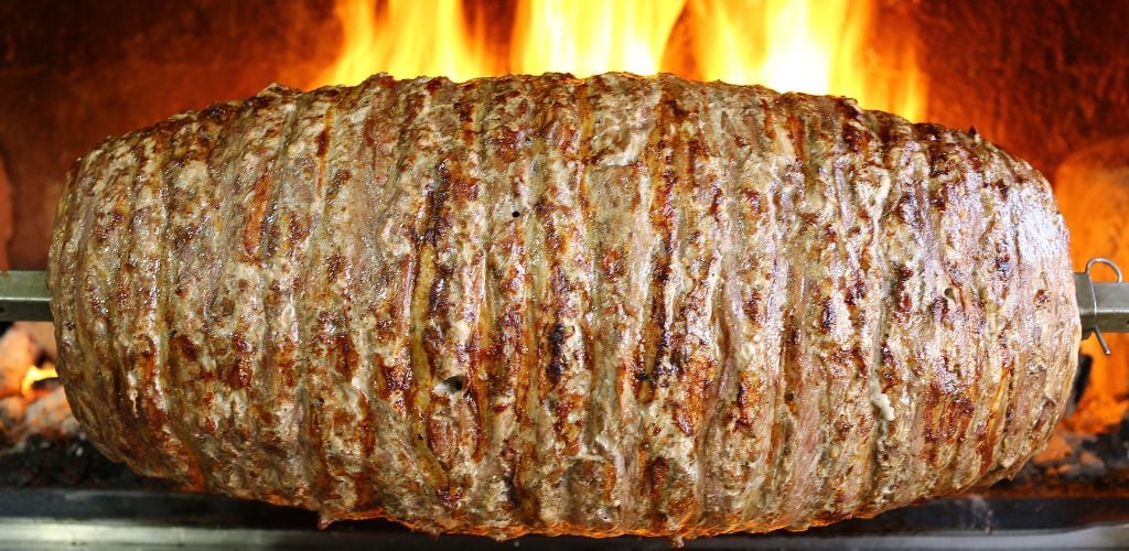 A large amount of meat cooked on a steel stick in a wood oven. 