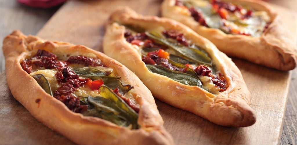 Turkish pides with vegetables on wooden cutting board. 