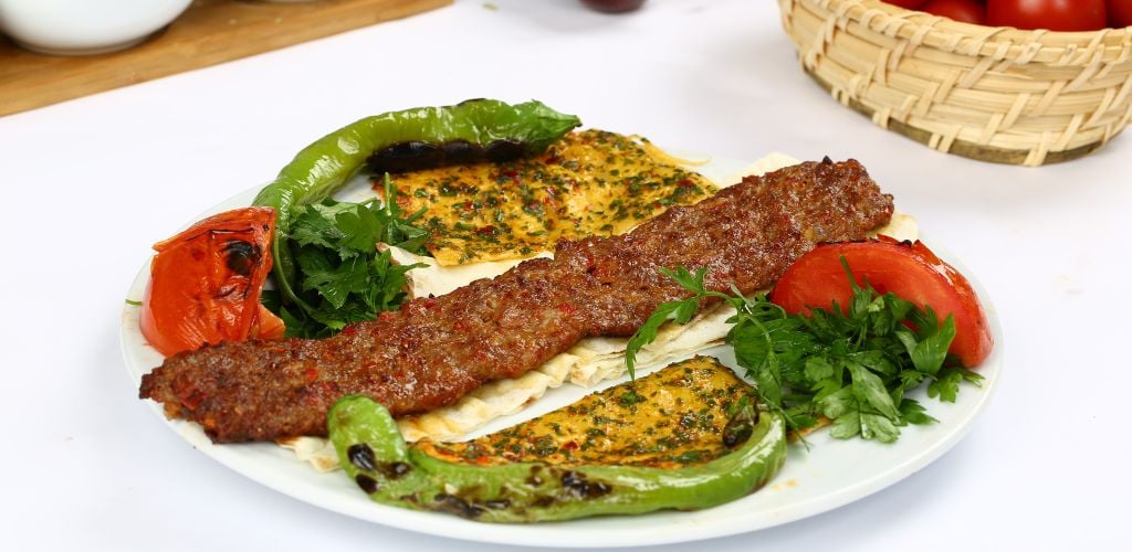 A meat shape on long, two grilled green peppers, grilled tomato, and scrambled egg on a white plate. 