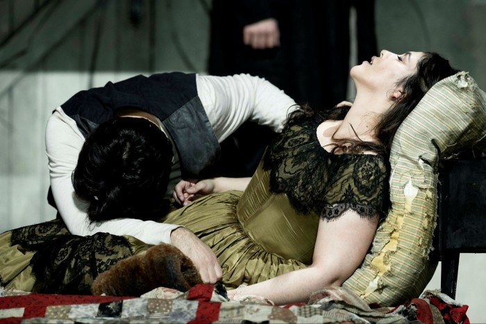 Leonardo Caimi as Rodolfo rests his head on the knees of an ailing Mimi (Yaritza Véliz) lying on chaise-longue in the Royal Opera House’s ‘La bohème’