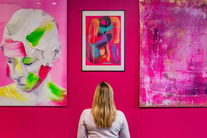 A woman looking up at three pink-hued paintings on a magenta wall at last year’s Affordable Air Fair