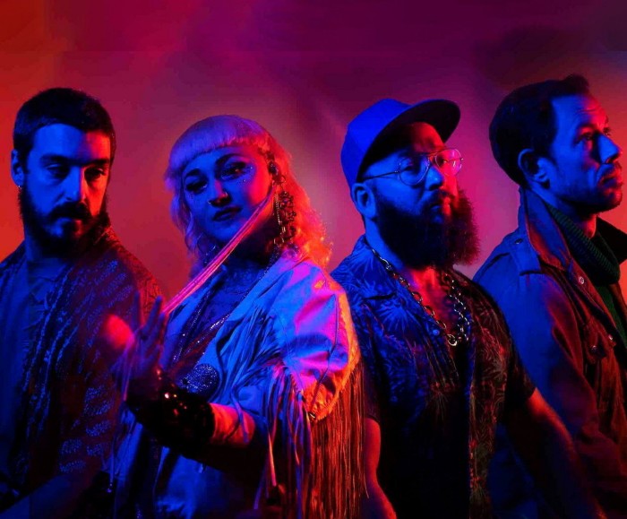 Three male and one female member of Hiatus Kaiyote standing in red and blue lighting