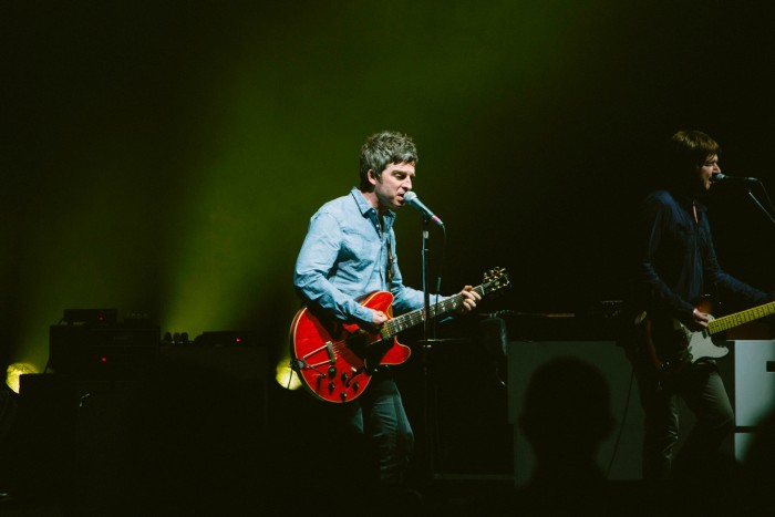 Noel Gallagher holding a red guitar on stage in Toronto