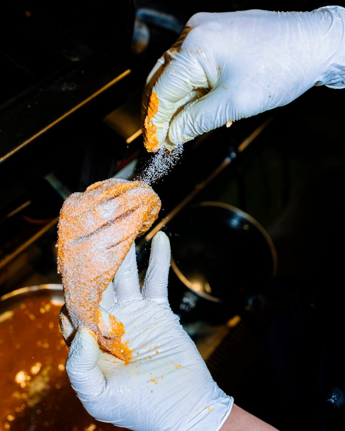 Two white-gloved hands seasoning sesame-crusted fish above a hob at Bangera’s Kitchen Ginza