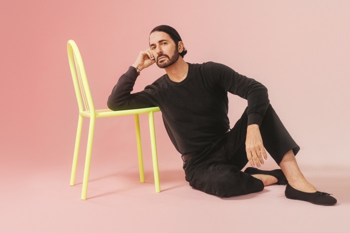 Marc Jacobs sits on the floor, resting one arm on a yellow chair next to him