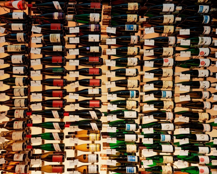 Rows of bottles of wine with labels hanging from their necks arranged horizontally on shelves at Crush Wine & Spirits