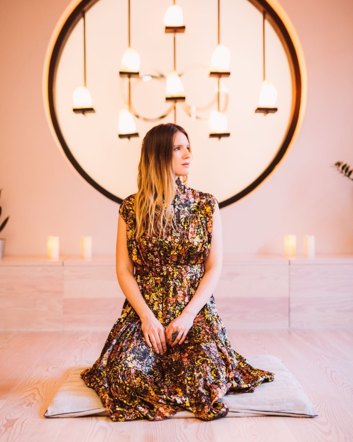 Re:Mind Studio founder Yulia Kovaleva kneeling on a mat in a pink-walled studio, in front of candles and a pendant lighting installation