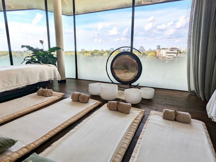 Four mats in a row, a bed, a gong surrounded by singing bowls in front of a floor-to-ceiling windows looking over London at Sound Bath Serenity