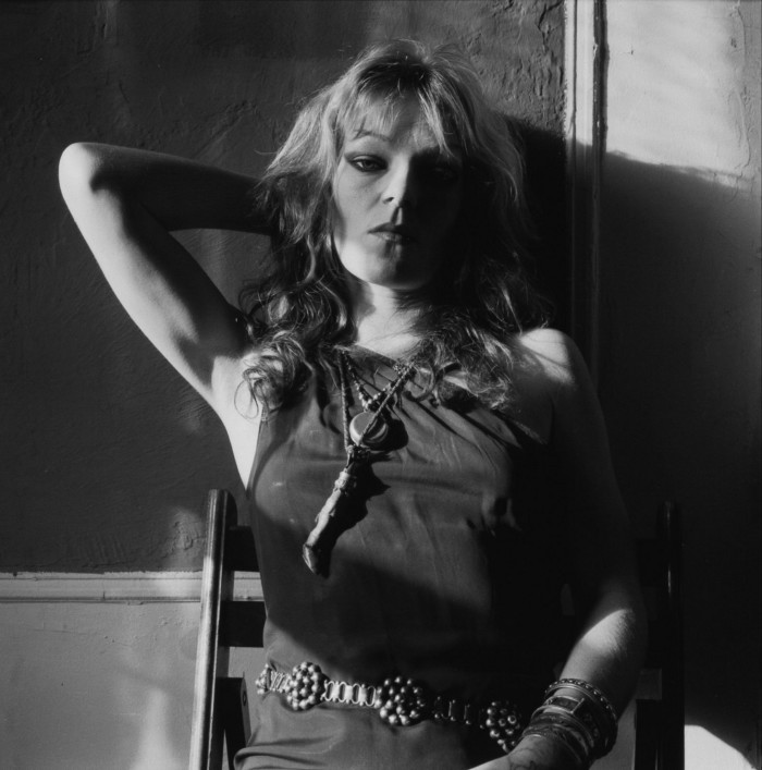 Actor and writer Cookie Mueller as photographed by David Armstrong: a black and white photograph from the 1970s of a woman with long blond hair leaning against a wall