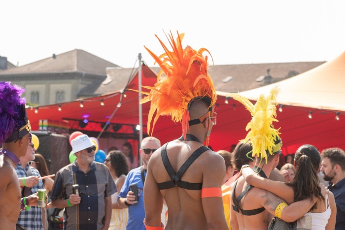 A man in an orange feather headdress and leather chest harness surrounded by other attendees of Zürich Pride 2023