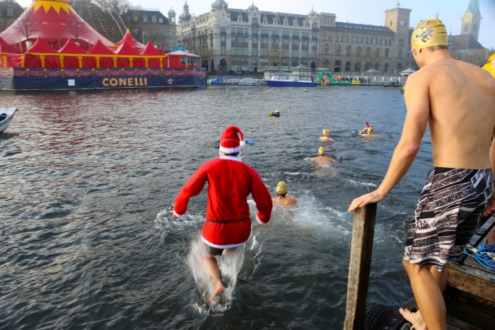 A man dressed as Santa Claus and other swimmers in yellow bathing caps in the River Limmat