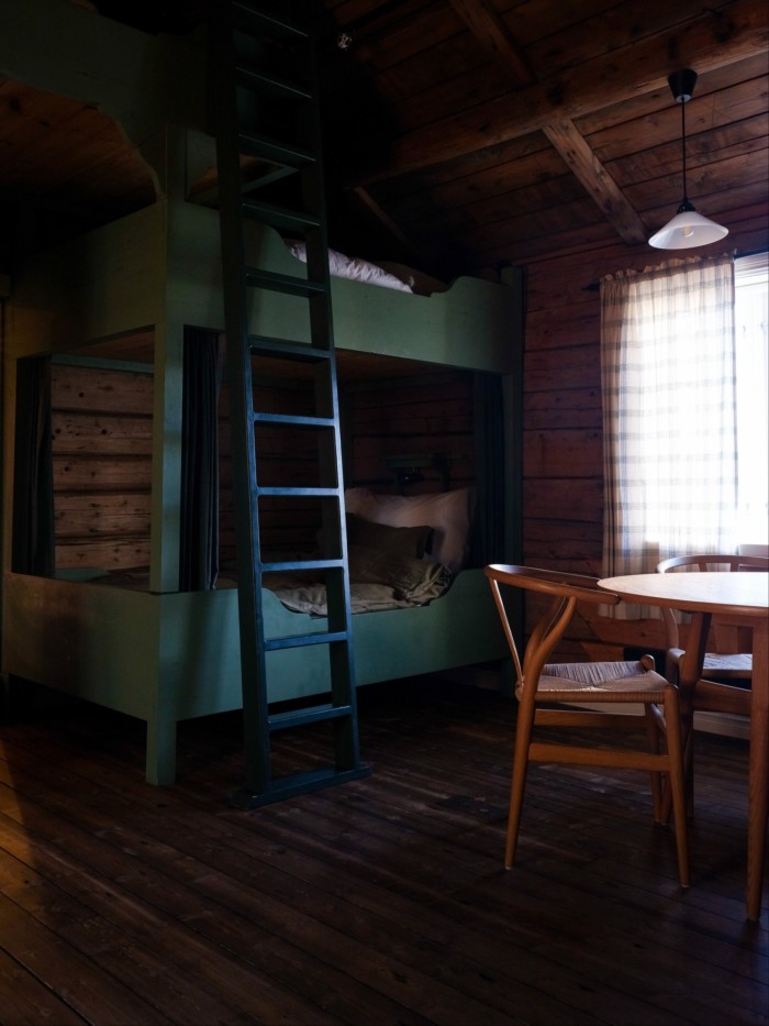 A bunk bed on top of another, with a ladder, in a room of wooden walls and ceiling