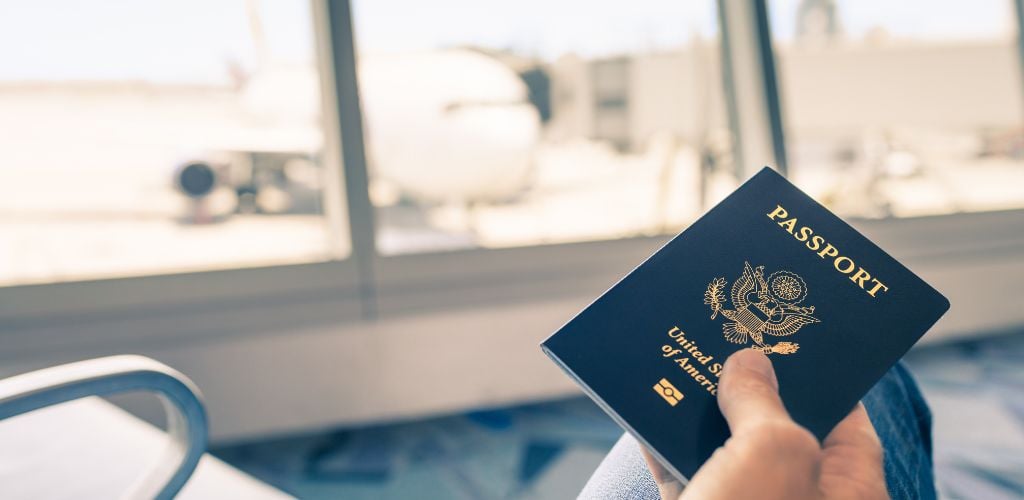 passport travel us passport, man in airport lounge holding passport, plane visible through the windows in background