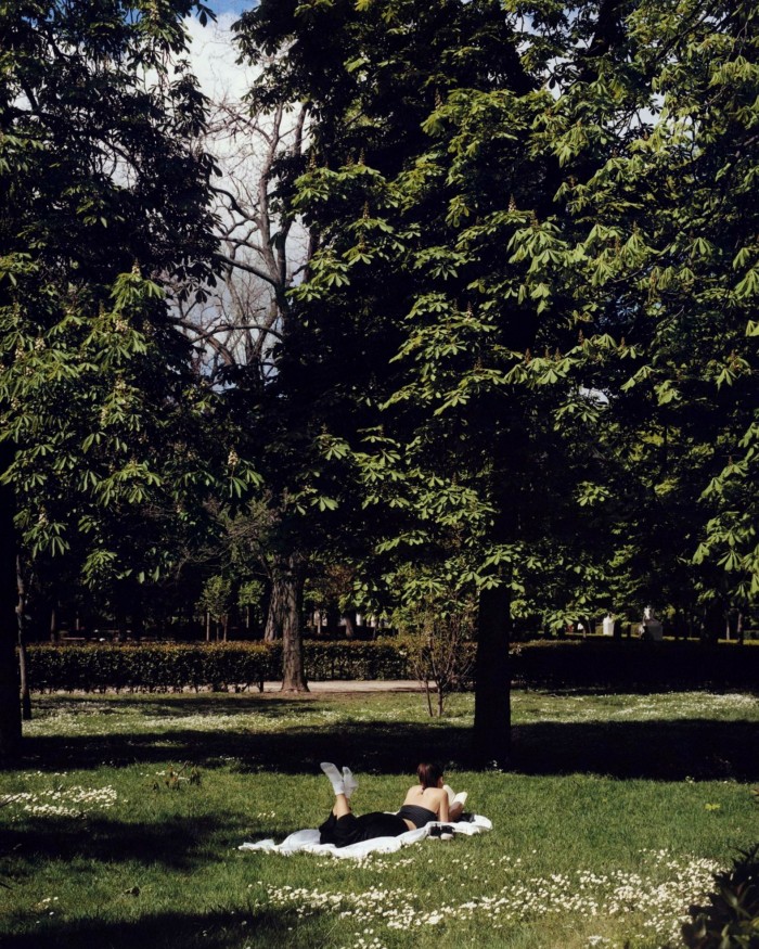  A female sunbather lying on a lawn surrounded by trees in El Retiro park