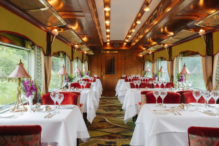 Tables in a rail carriage are draped with white linen tablecloths. Glasses and cutlery are laid out ready for a meal 