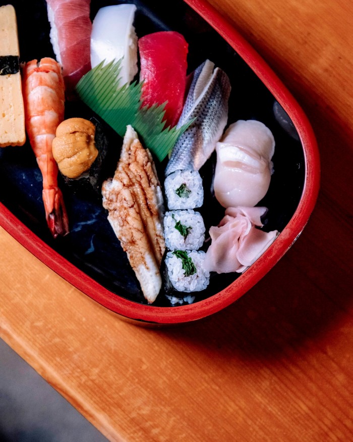 A selection of Okuzumi’s nigiri in a red and black oval tray on a wooden table