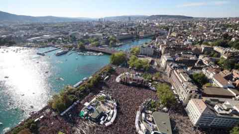 An aerial photograph of thousands of people at Zürich’s Street Parade, the city’s annual techno party, on the edge of the lake