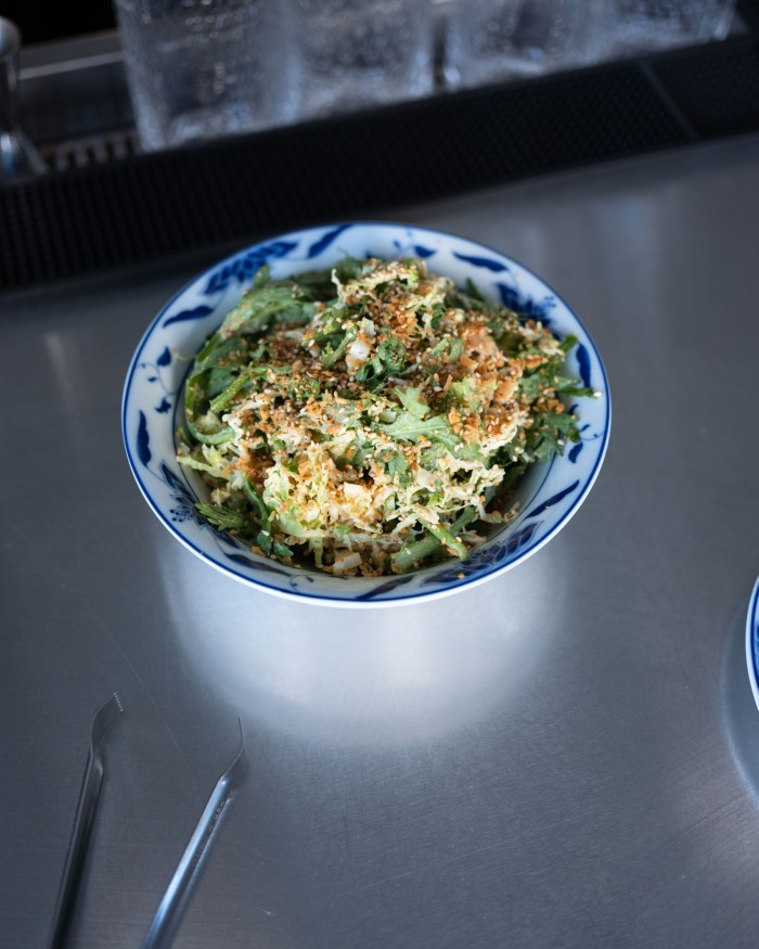 A small blue and white bowl of chrysanthemum greens on a metallic surface
