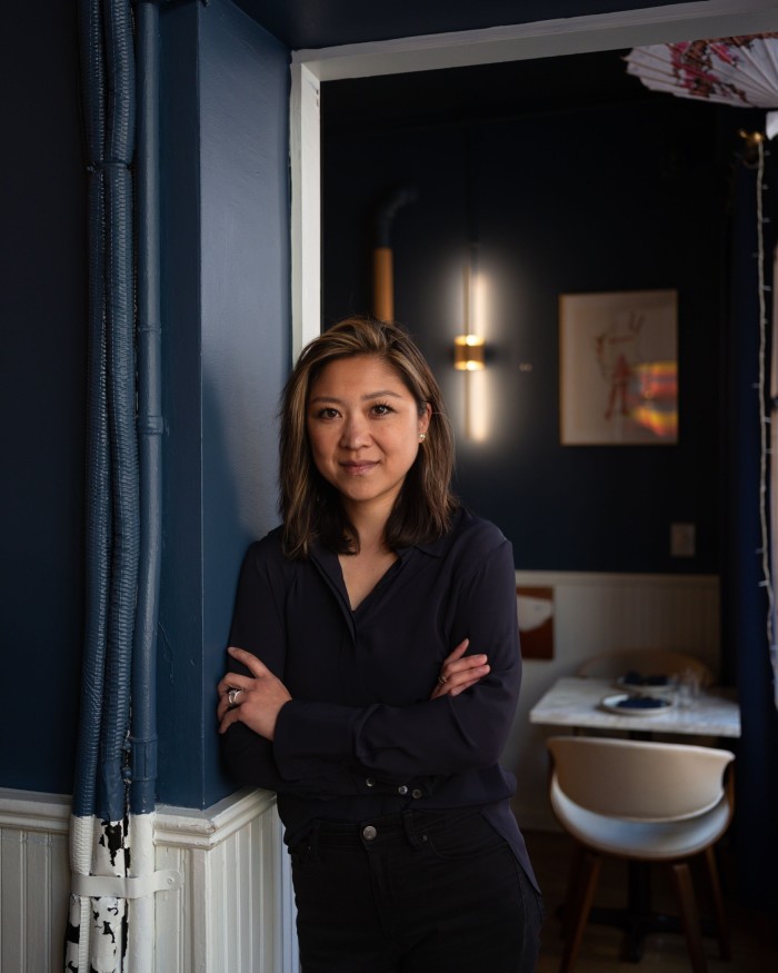 Figure Eight owner Emmeline Zhao, leaning against a blue wall by a doorway in her restaurant
