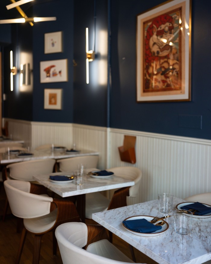 A row of small marble tables for two in Figure Eight’s dining space, against a white and blue wall