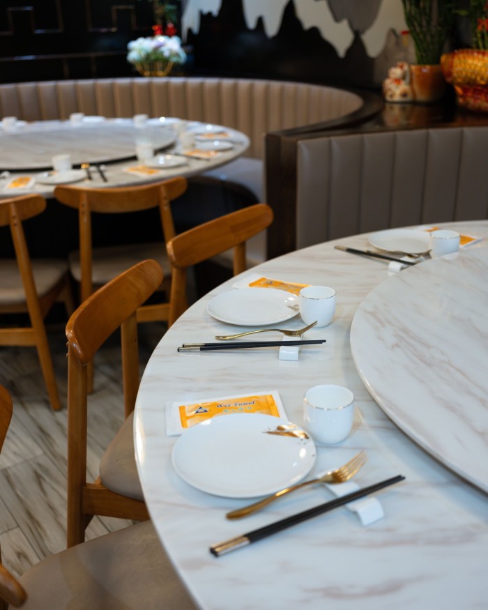 Large white marble tables and circular brown leather booths in Hakka Cuisine