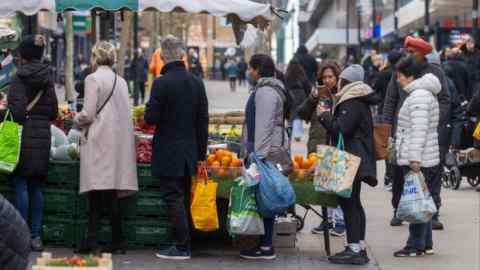 Shoppers queue at a fruit and vegetable stall in London