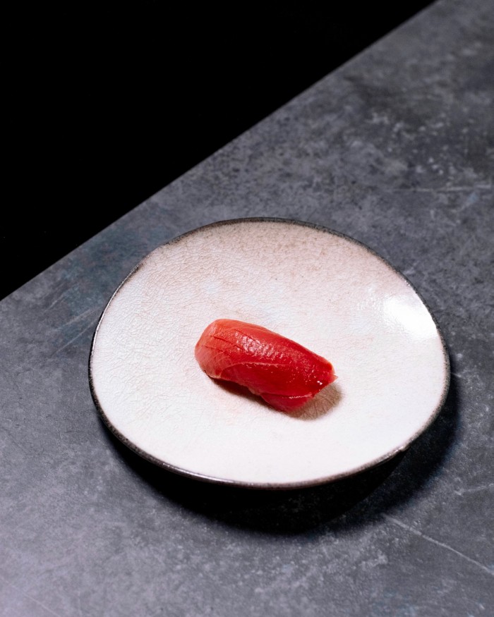 A small white round plate with a piece of maguro (tuna) nigiri on it at Sushi Yuko