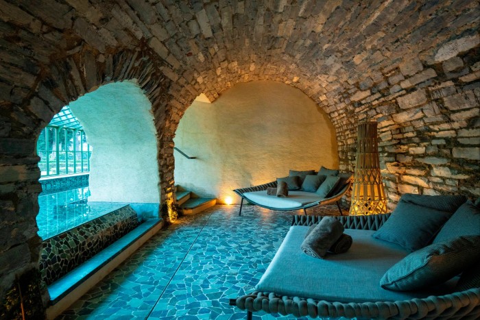 Wide blue armchairs in a vault like room with a view through arches to a swimming pool