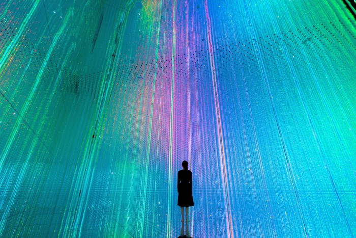 The silhouette of a woman in a teamLabs installation standing in front of green and purple shards of light