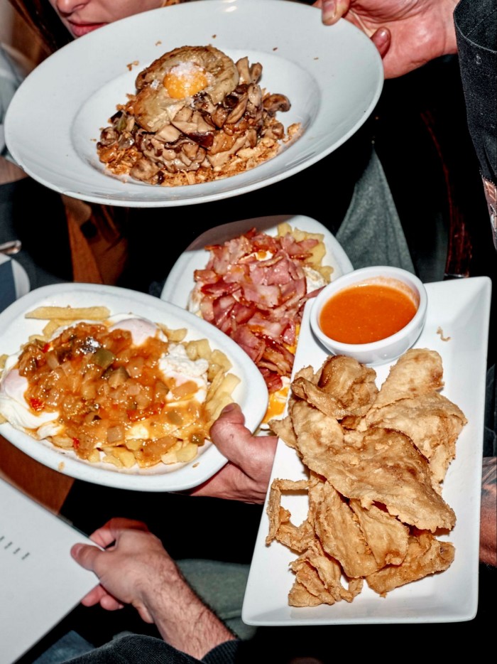 Hands holding plates of egg-based dishes and a tray of deep-fried tapas at Los Huevos de Lucio