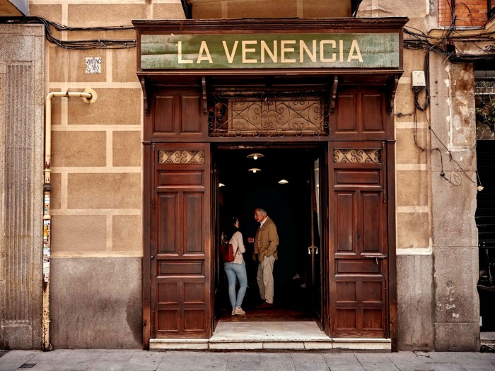 A man and a woman standing just outside the dark-wood entrance of La Venencia