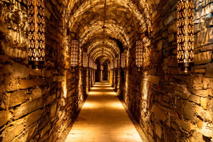 A brick tunnel illuminated by lanterns that cast pattern shadows