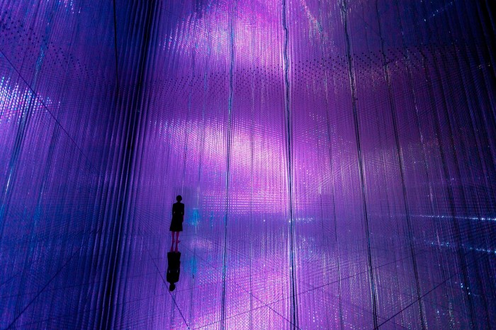 The Infinite Crystal Universe, an installation by Tokyo’s teamLab Planets: the silhouette of a woman standing on a mirrored floor in front of mirrored walls filled with purple lights 