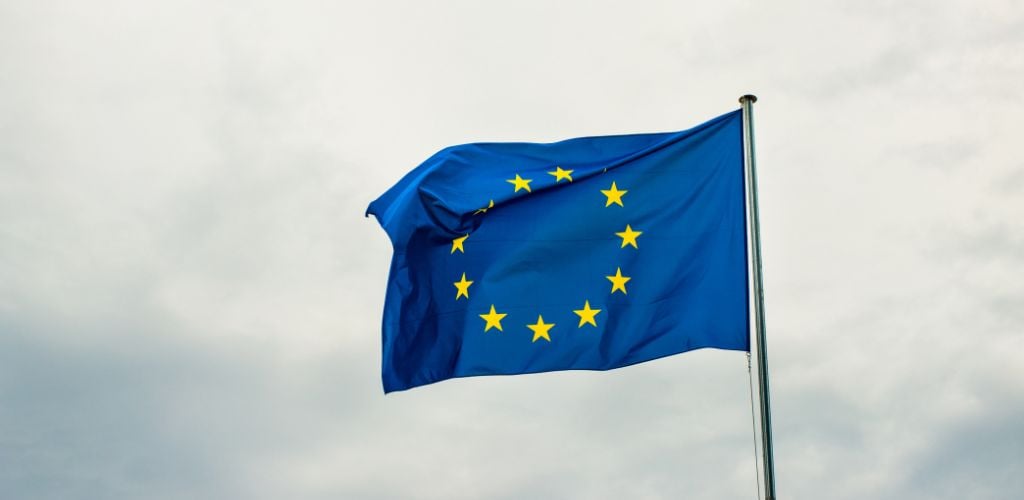 European flag, blue with yellow stars forming a circle, hoisted high on pole 