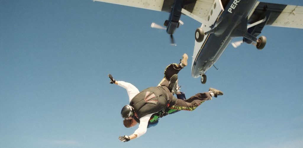 skydive image, shortly after jumping out of plane. Plane visible above, two people in tandem free-falling before parachute launch