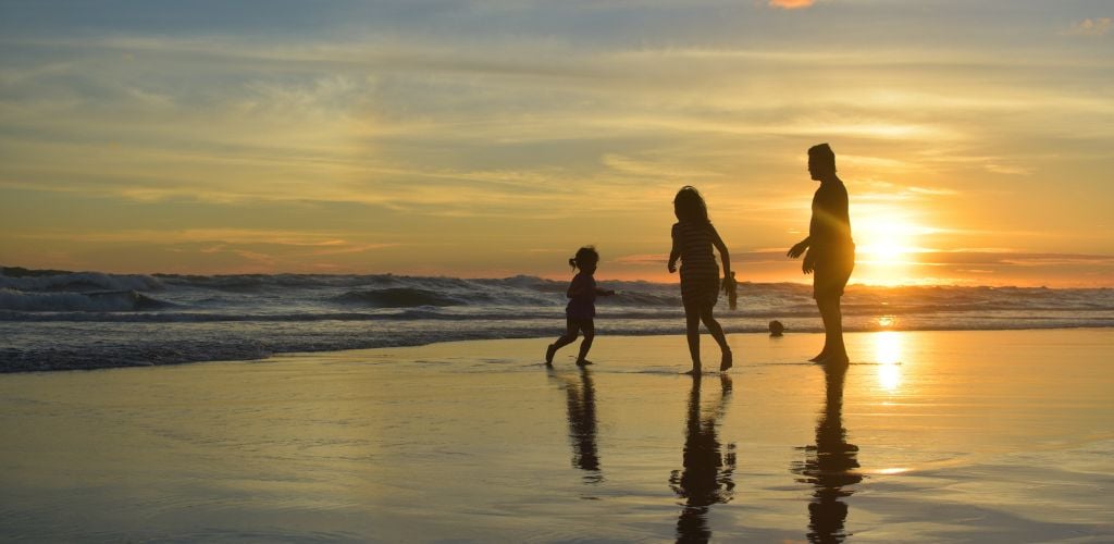 silhouette of family playing in waves on beach during sunset hour 