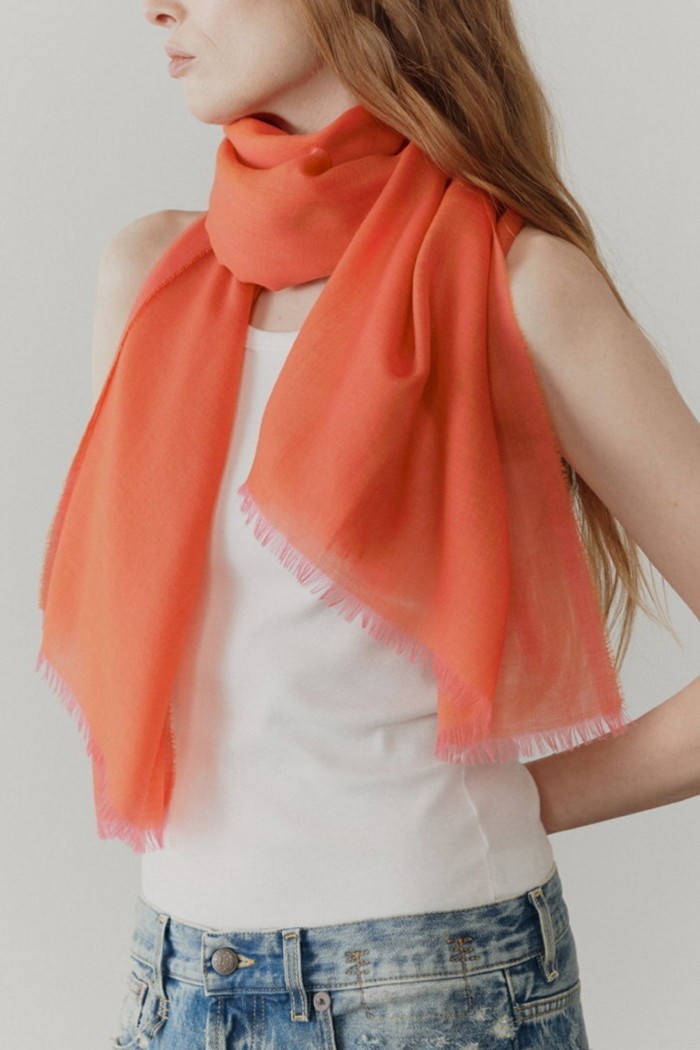 A model wears an orage scarf over a white sleeveless top and jeans