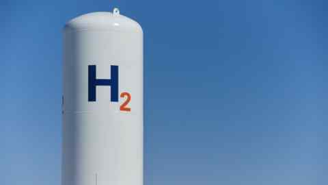 A large white cylindrical tank with the symbol “H2” written in blue and orange, set against a clear blue sky