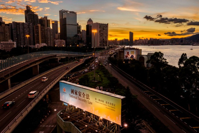 A large illuminated billboard by a flyover, with highrise buildings in the distance