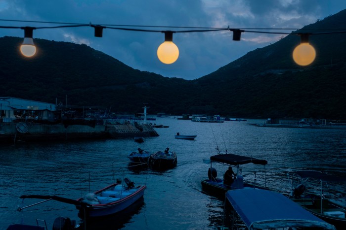 Lanterns glow at dusk, with small boats on the water in front