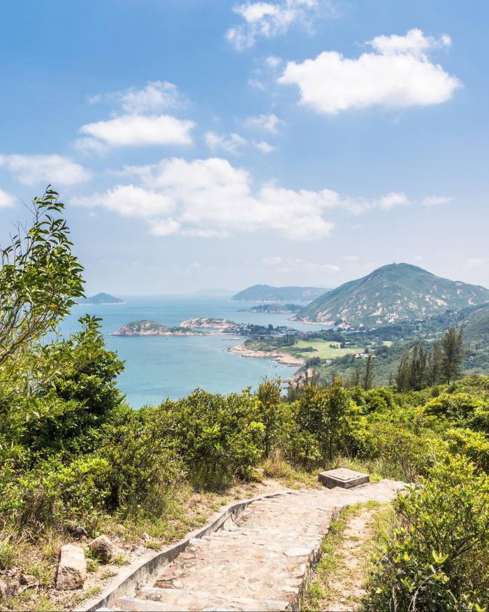 A path at the end of Hong Kong’s Dragon’s Back trail, flanked by greenery and with sea and hills in the distance