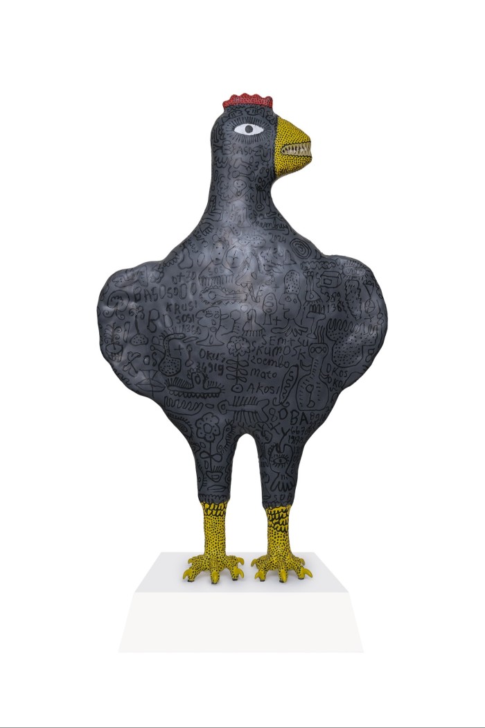 A ceramic sculpture of a large fierce-looking black chicken with words and cartoony characters inscribed
