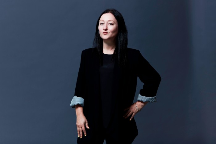 A woman with long black hair wearing a black jacket looks purposeful