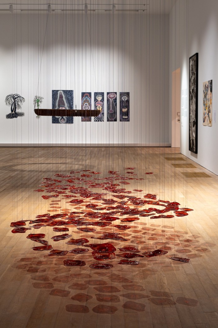 Red glass pieces hang from wires in a snakelike pattern and cast shadows on the floor
