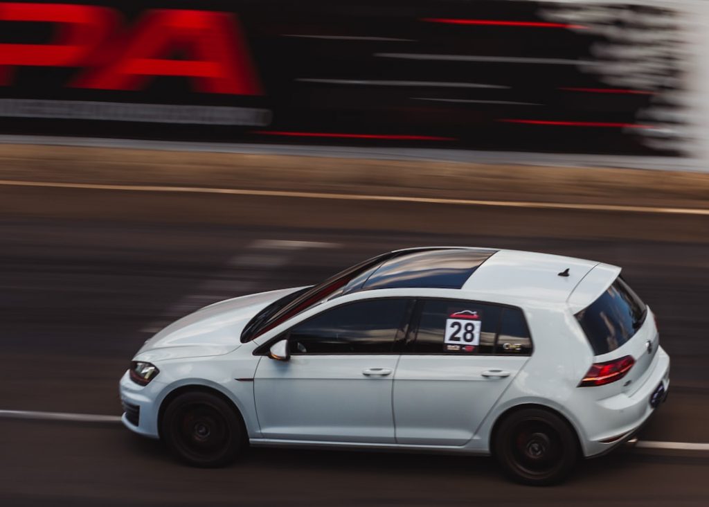 White Volkswagen Golf GTI racing on track, side view, showcasing its speed and performance in the context of its historical evolution.