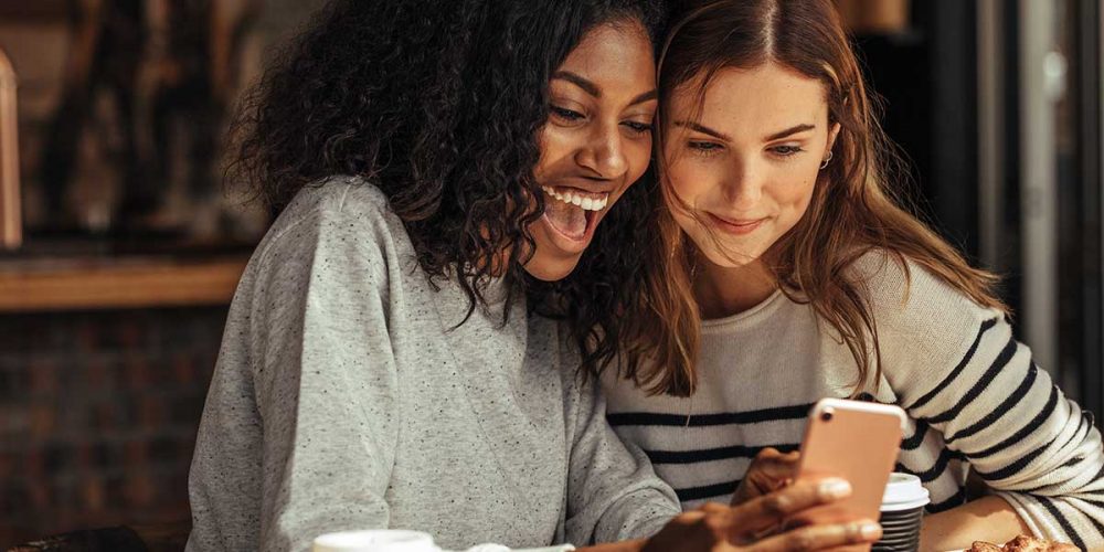 friends-scroll-through-mobile-phone-in-cafe