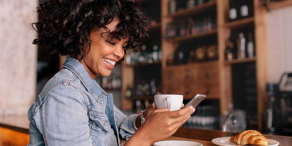 woman-smiles-at-mobile-phone-whilst-drinking-coffee