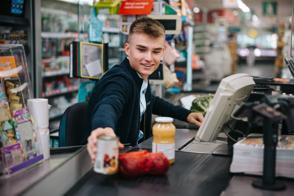 Man serving customers at supermarket checkout. Male sales clerk scanning products at grocery store checkout.