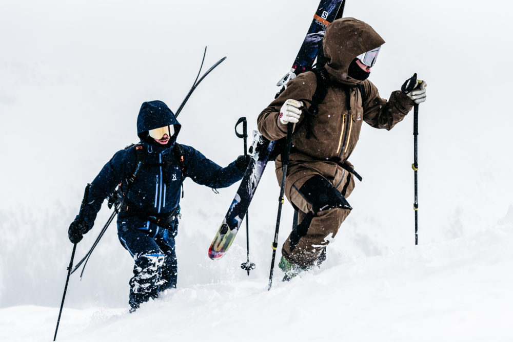 Two people walking up a snowy hill with skis. Haglöfs Winter 2021.
